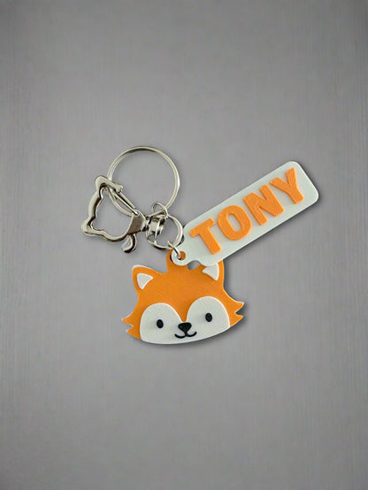 Keychain with fox design and 'TONY' tag on a wooden surface